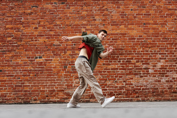 Motion shot de hombre joven bailando hip-hop al aire libre contra la pared de ladrillo, espacio de copia - Foto, imagen