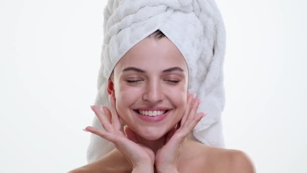 Valkoihoinen nainen, jolla on pyyhe pään ympärillä, hymyilee aidolla onnellisuudella puhtaan valkoisen taustan edessä. Hänen rento ja sisällöllinen ilmeensä säteilee positiivisesti. - Materiaali, video