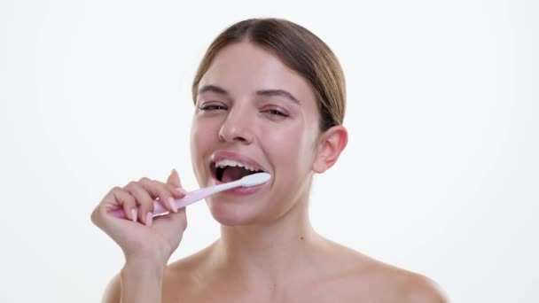 La donna caucasica pulisce i denti con un sorriso radioso, mostrando con entusiasmo l'importanza dell'igiene orale. Sullo sfondo bianco, la felicità aggiunge un tocco di positività alla cura dentale. - Filmati, video