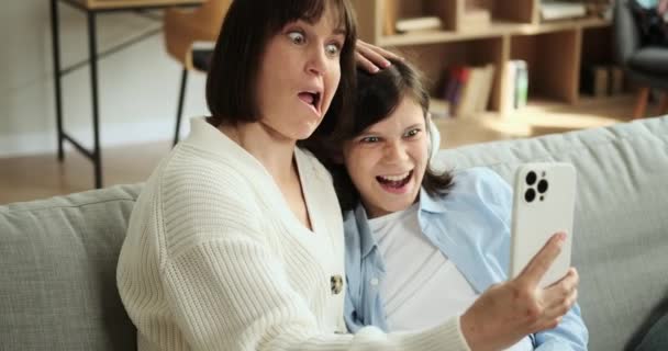 Anya és fia megosztják játékos pillanataikat, telefonálgatnak, miközben a kanapén ülnek. Nevetésük és gondtalan gesztusaik a családi szórakozás és összetartás szívmelengető színterét hozzák létre.. - Felvétel, videó