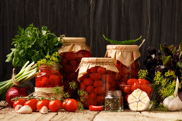 Tomates cerises en conserve dans un bocal fermé, épices et herbes pour la marinade sur un fond de bois rustique. - Photo, image