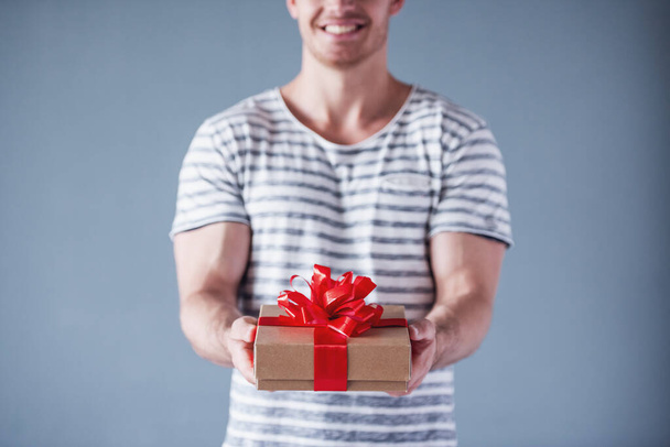 Rajattu kuva komea nuori mies tilalla lahjapakkauksessa ja hymyilee, harmaalla pohjalla
 - Valokuva, kuva