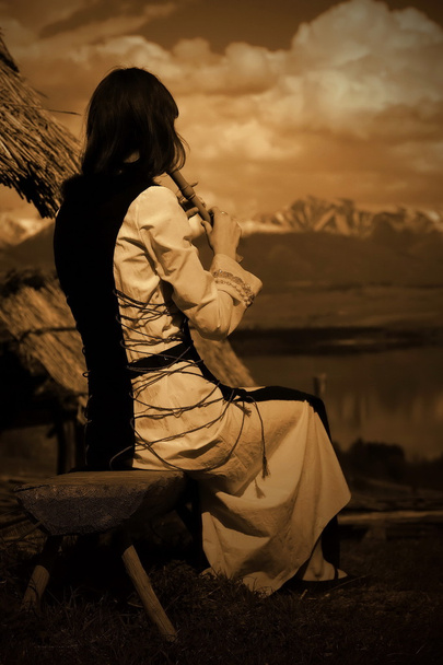 Una hermosa chica en un traje histórico tocando su flauta en un paisaje abierto con un lago
 - Foto, imagen