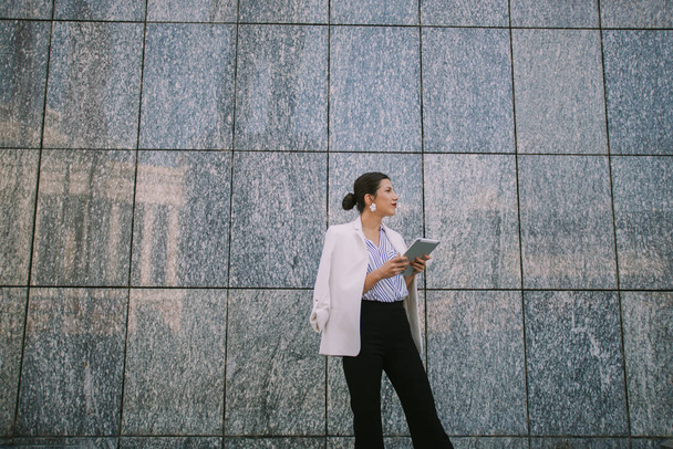 Mulher de negócios bonita olhando para longe, enquanto em pé na frente da parede - Foto, Imagem