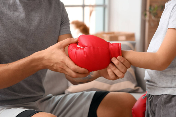Young man and his little son with boxing glove at home, closeup - Photo, Image