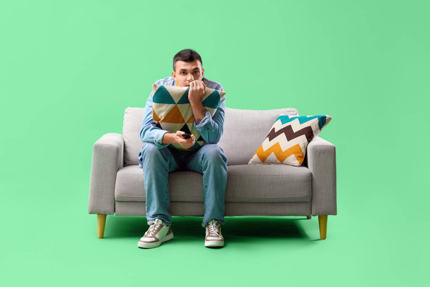 Νεαρός άνδρας βλέποντας τηλεόραση στον καναπέ σε πράσινο φόντο - Φωτογραφία, εικόνα