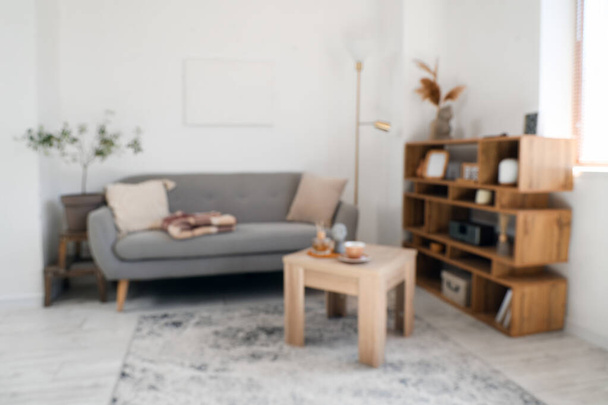 Vista sfocata del soggiorno con divano grigio, coperta calda e tazza di tè sul tavolino - Foto, immagini