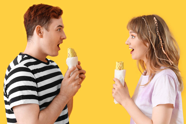 Sorprendida pareja joven con sabrosas envolturas de sándwich sobre fondo amarillo - Foto, imagen