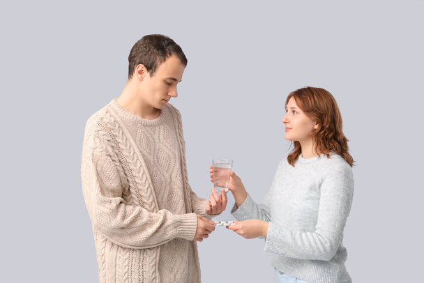 Ill jonge man het nemen van pillen en water van vriendin op lichte achtergrond - Foto, afbeelding