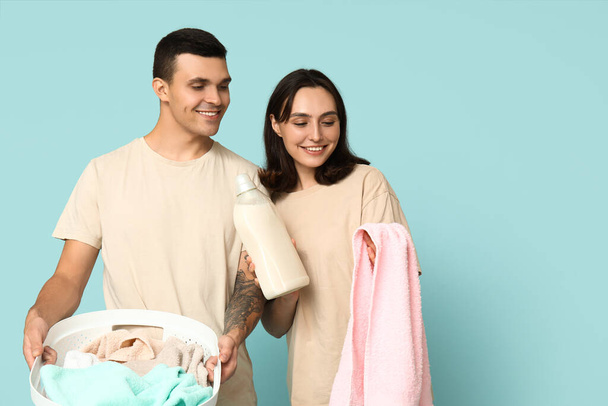 Young couple with laundry basket and bottle of detergent on blue background - Photo, Image