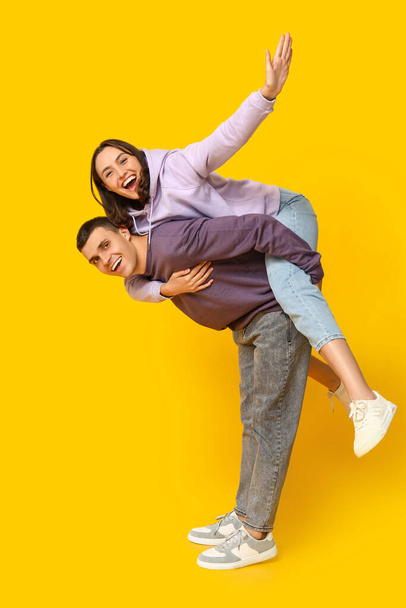 gelukkig jongeman geven piggyback rit naar zijn vriendin op gele achtergrond - Foto, afbeelding