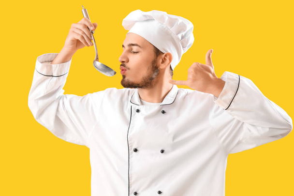 Chef masculino con cucharón mostrando gesto de "llámame" sobre fondo amarillo - Foto, imagen