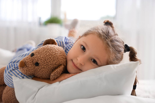 Милая маленькая девочка с игрушечным мишкой в спальне, крупным планом - Фото, изображение