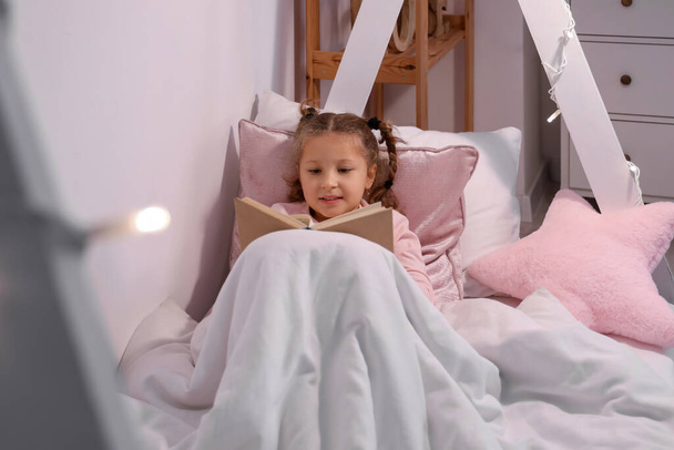 Geceleri yatak odasında kitap okuyan tatlı küçük bir kız. - Fotoğraf, Görsel