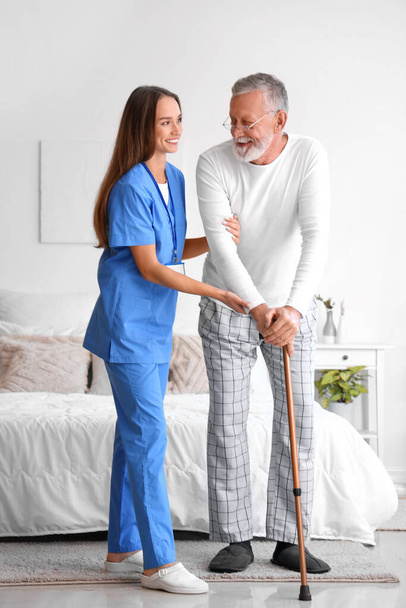 Női gondozó segít idősebb férfi sétabot a hálószobában - Fotó, kép
