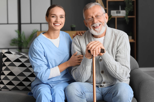 Senior man met stok en verpleegster thuis - Foto, afbeelding
