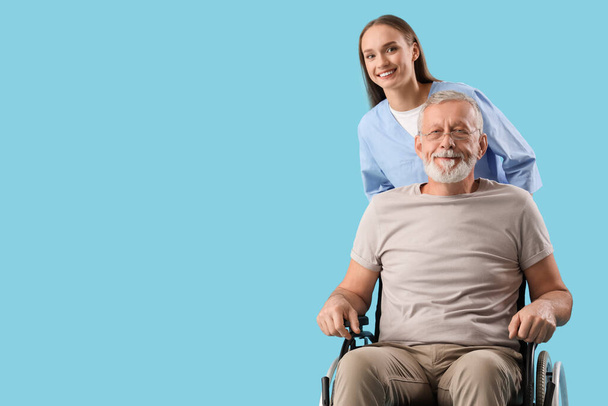 Uomo anziano in sedia a rotelle con infermiera su sfondo blu - Foto, immagini
