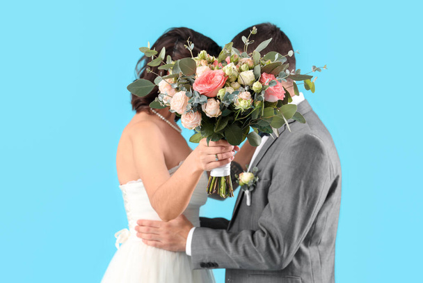 青い背景に花束を持つ若い結婚式のカップル - 写真・画像