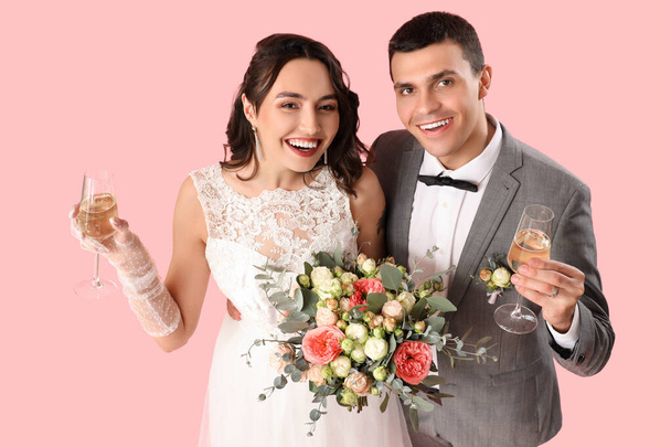 Junges Hochzeitspaar mit Blumenstrauß und Champagner auf rosa Hintergrund - Foto, Bild