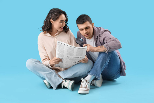 Young couple with newspaper and magnifier on blue background - Photo, Image