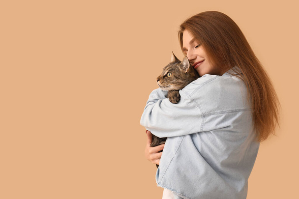 Pretty young woman with cute tabby cat on beige background - 写真・画像