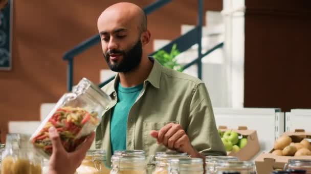 Prodejce prezentuje své ekologické produkty veganskému klientovi, nakupuje potraviny, ukazuje omáčky a zásoby do spíže v lahvích nebo sklenicích. Zákazník přemýšlí o nákupu čerstvých přírodních potravin. - Záběry, video