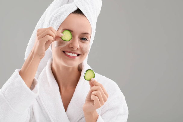 Woman with cosmetic product on her face and cucumber slices against grey background, space for text. Spa treatments - Fotó, kép
