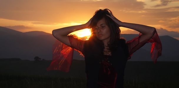 Krásná víla dívka v historické kostýmy s dlouhou průhledné rukávy a expresivní gesto v krajině večer zapadajícího slunce - Fotografie, Obrázek