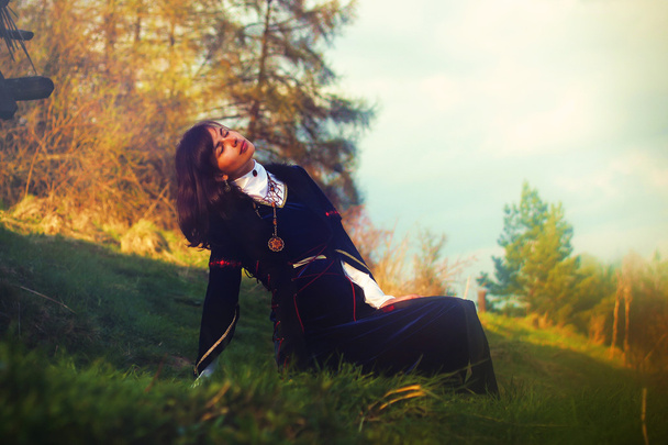 Una bella giovane donna con i capelli scuri e un abito storico in posa su un prato in un paesaggio aperto
 - Foto, immagini