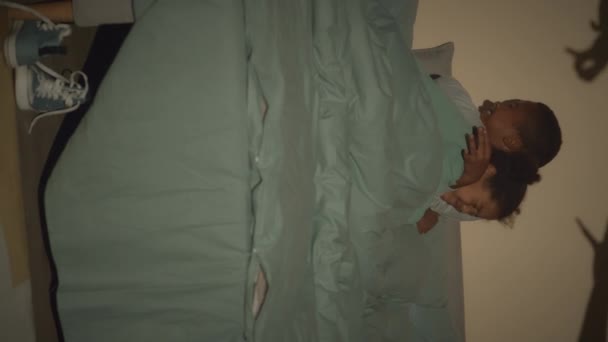 Vertikale Verlangsamung zweier afroamerikanischer kleiner Bruder und Schwester, die sich umarmen, während sie Angst vor Monstern in ihrem Zimmer haben, die ein Schattenspiel an der Wand spielen - Filmmaterial, Video