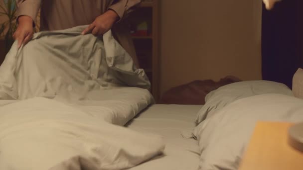 Recortado disparo de la abuela afroamericana poniendo dos nietos entre sí vistiendo pijamas acogedores a la cama, cubriéndolos con suave manta caliente - Metraje, vídeo