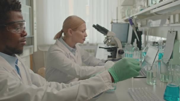 Kallistaa alas kaksi monipuolista mies ja nainen kemistit yllään valkoinen lab takit suorittaa kokeita nestemäisten aineiden laboratoriossa - Materiaali, video