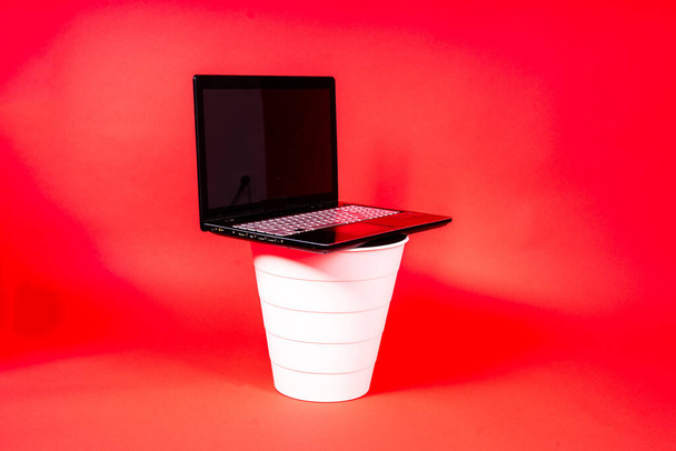 Zwarte laptop in een prullenbak op rode achtergrond geïsoleerd - Foto, afbeelding