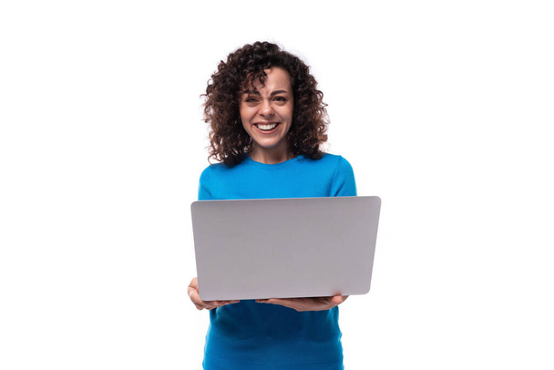 νέα σγουρή γυναίκα με μαύρα μαλλιά φοράει ένα μπλε εταιρική t-shirt και κρατώντας ένα φορητό υπολογιστή. - Φωτογραφία, εικόνα