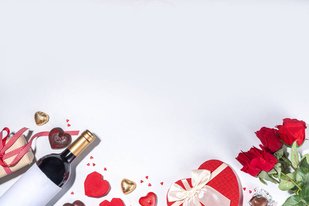 Valentine's Day greeting card flat lay. Valentine day isolated white background with wine bottle, heart sweets chocolates, bouquet of red roses, gift box, heart shaped candies, confetti, beads  - Foto, afbeelding