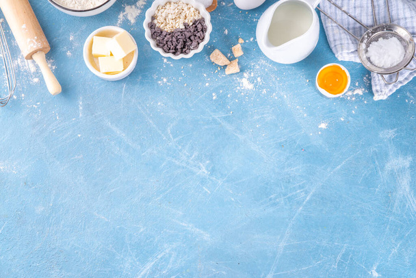Baking ingredients background. Cooking ingredients (flour, eggs, milk, brown sugar, butter) with utensils on light blue background top view copy space - Fotó, kép