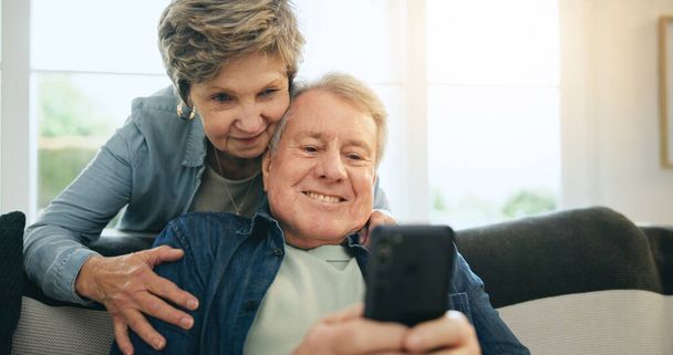 Senior, couple and hug with phone or happy for social media, streaming or internet scroll on sofa of living room. Elderly, woman and man with smartphone on couch in lounge for digital app and smile. - Foto, Imagen