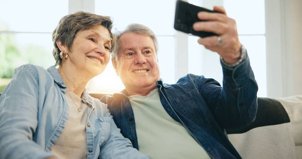Счастливая пожилая пара, селфи и диван в гостиной, чтобы сфотографироваться, на память или сфотографироваться вместе дома. Зрелый мужчина или женщина улыбаются в релакс для фотографии, видео или социальных медиа в пенсии в доме. - Фото, изображение