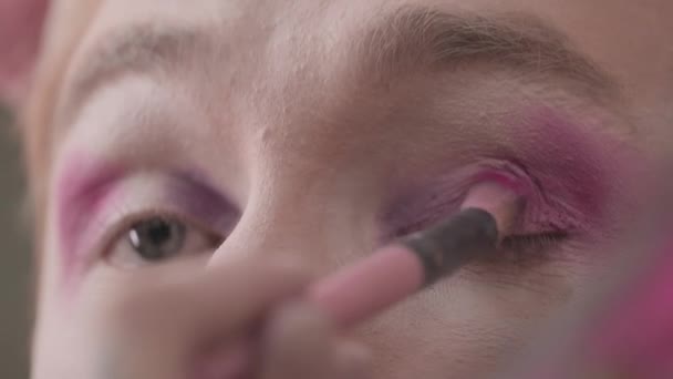 Close-up van jonge blanke queer man doet gradiënt roze oog make-up terwijl het maken van klaar voor drag show - Video