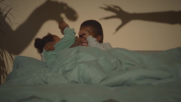 Slowmo de dois afro-americanos tween irmãos deitados juntos sob cobertor na cama no quarto escuro e gritando com sombras assustadoras na parede jogando seu jogo - Filmagem, Vídeo