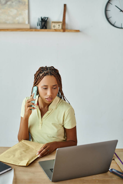 bella donna africana americana parlando per telefono con pacchetto postale in mano e guardando il computer portatile - Foto, immagini