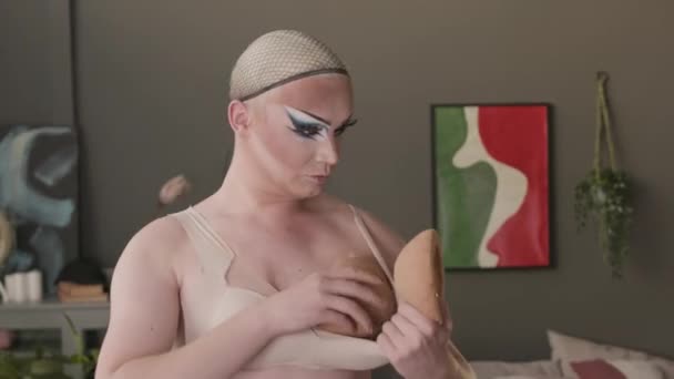 Vita di uomo queer caucasico con impressionante trucco trascinamento utilizzando cuscinetti reggiseno push-up per fare seni finti mentre si vestiva per lo spettacolo di trascinamento a casa - Filmati, video