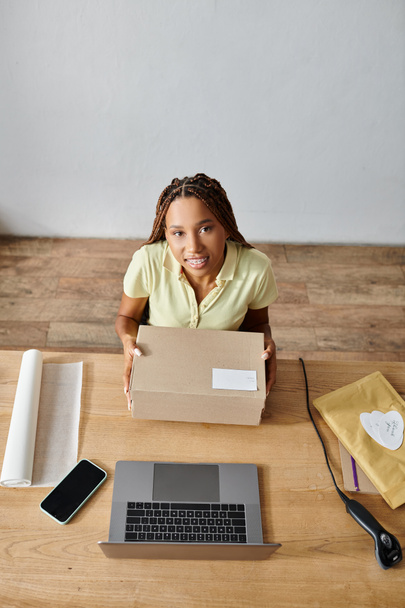 cheerful young african american female retailer holding box and looking at camera, delivery concept - Photo, Image