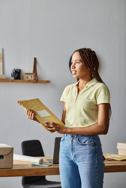 attrayant travail dur vendeur afro-américain femme tenant des paquets de courrier et détournant les yeux - Photo, image