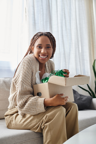pretty jolly african american woman with braces holding box with green shoes and smiling at camera - Photo, Image