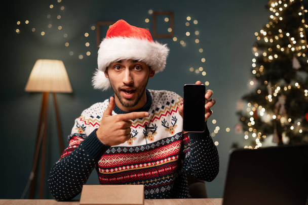 Vlogger tekee purkaminen tarkastelu video matkapuhelimen esittäessään kameralle. Sosiaalisen median vaikuttaja Santa hattu unboxing älypuhelin jouluna. Kopioi tila - Valokuva, kuva