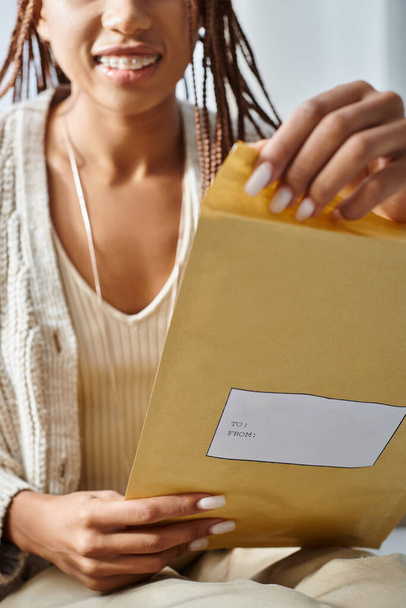 обрезанный вид с акцентом на пост-пакет в руках размытой веселой африканской американки с брекетами - Фото, изображение