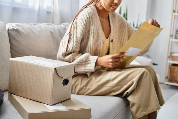 vista recortada con foco en cajas de cartón al lado de la mujer afroamericana borrosa con paquete de correos - Foto, Imagen