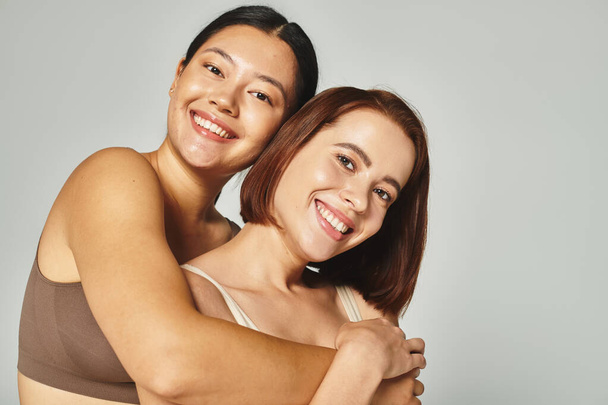alegre asiático mulher no cueca abraçando seu jovem amigo no cinza fundo, companheirismo - Foto, Imagem