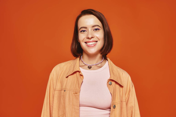 cheerful young woman with short hair looking at camera and smiling on orange background, carefree - Foto, imagen
